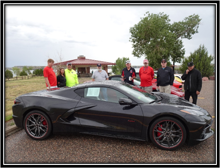 A group of people standing around a black sports car

Description automatically generated