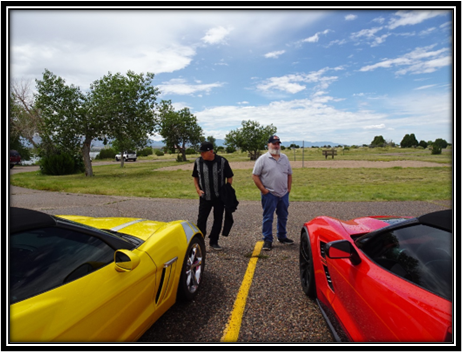 Two men standing next to a red sports car

Description automatically generated