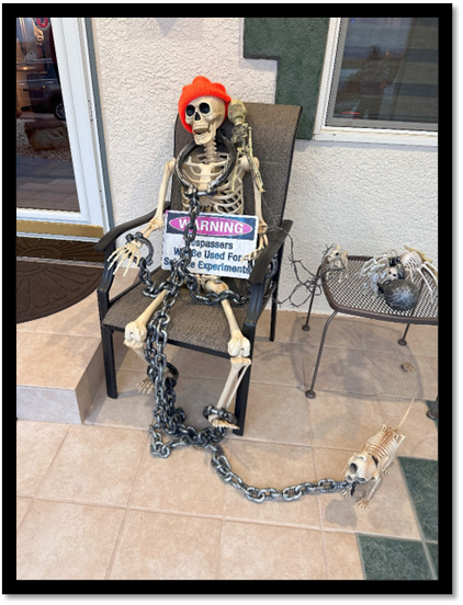 A skeleton sitting in a chair with a sign and chain

Description automatically generated