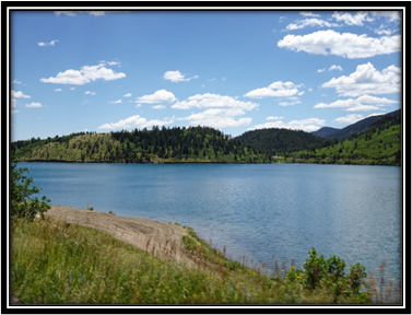 A lake with a grassy hill and trees

Description automatically generated