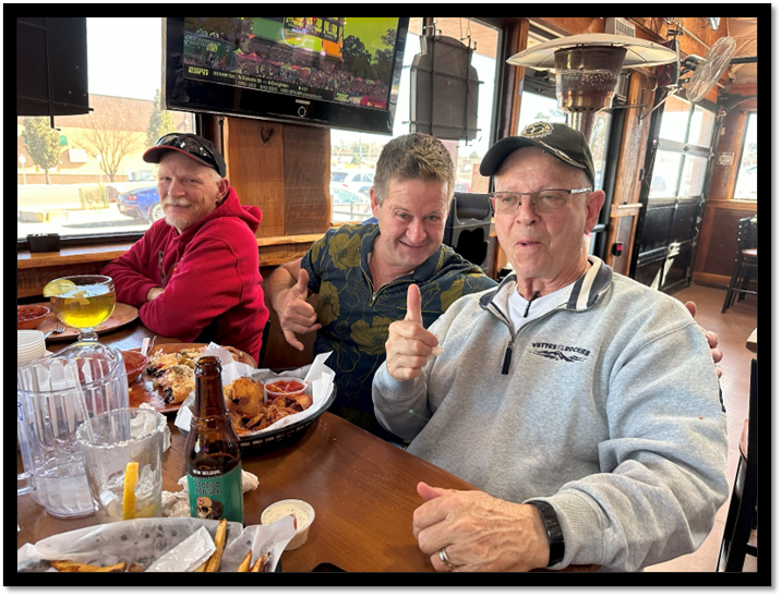 A group of men sitting at a table with food and drinks

Description automatically generated