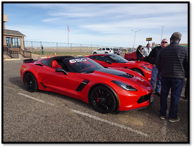 A red sports car parked on a gravel road with people standing around

Description automatically generated with low confidence